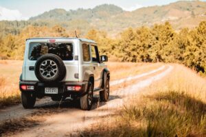 An off-road vehicle driving through a picturesque countryside path with mountains in the background.