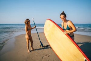 Two women prepare paddleboards on a sunny beach in Vietnam, showcasing a vibrant and adventurous lifestyle.